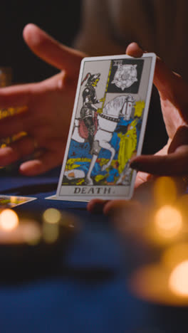 Video-Vertical-Cerca-De-Una-Mujer-Dando-Lectura-De-Cartas-Del-Tarot-En-Una-Mesa-A-La-Luz-De-Las-Velas-Sosteniendo-La-Carta-De-La-Muerte-1